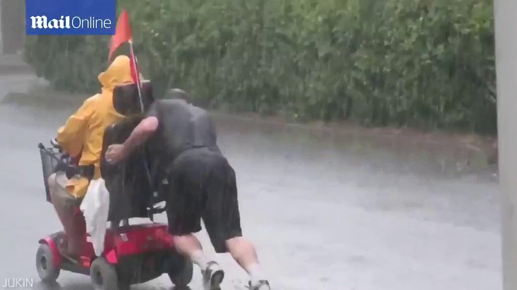 Một em bé đang gắng sức giúp người đàn ông ngồi xe lăn lên vỉa hè.