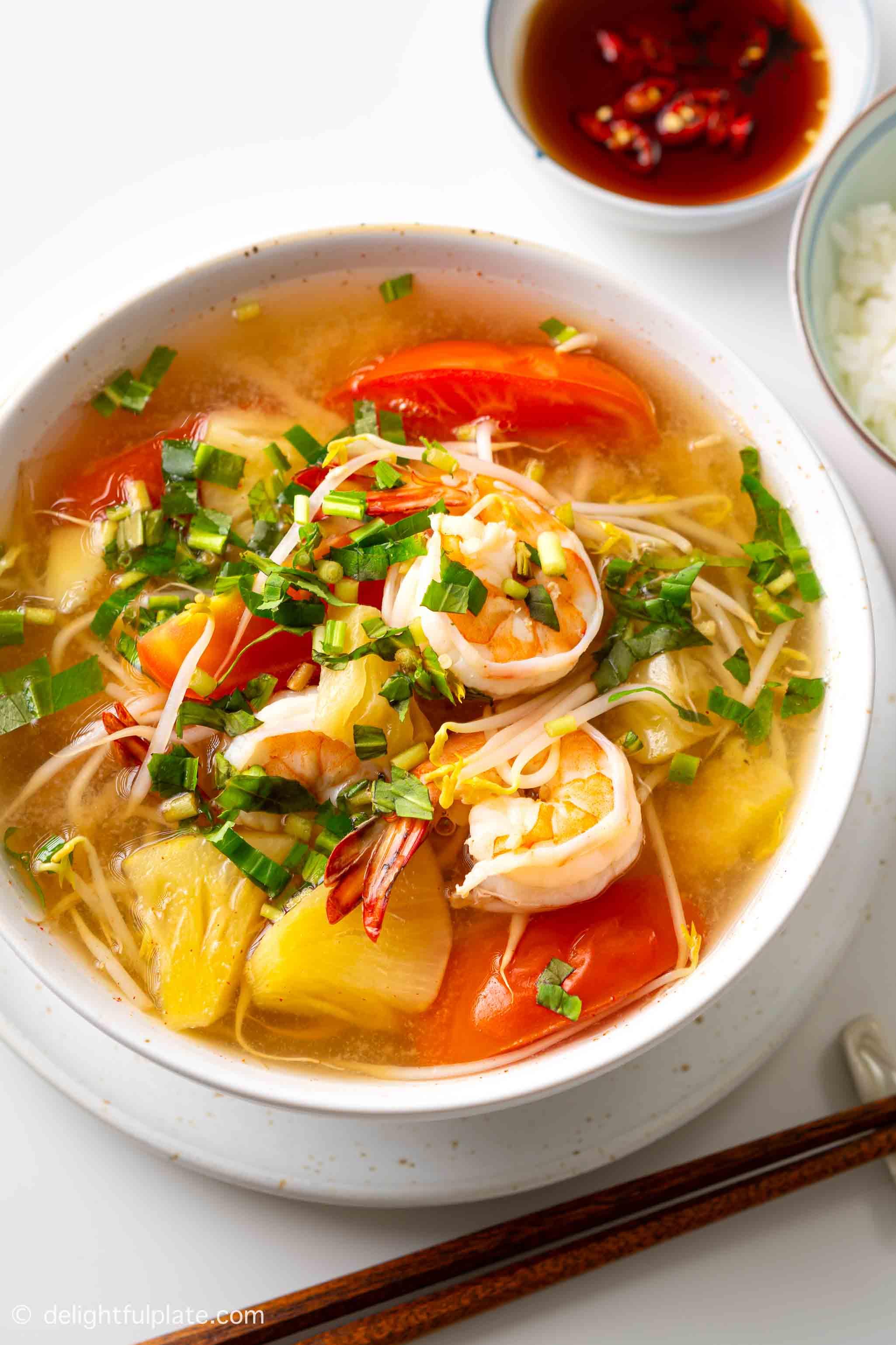 a bowl of Vietnamese sour shrimp soup (Canh chua tôm) with rice and fish sauce on the side.